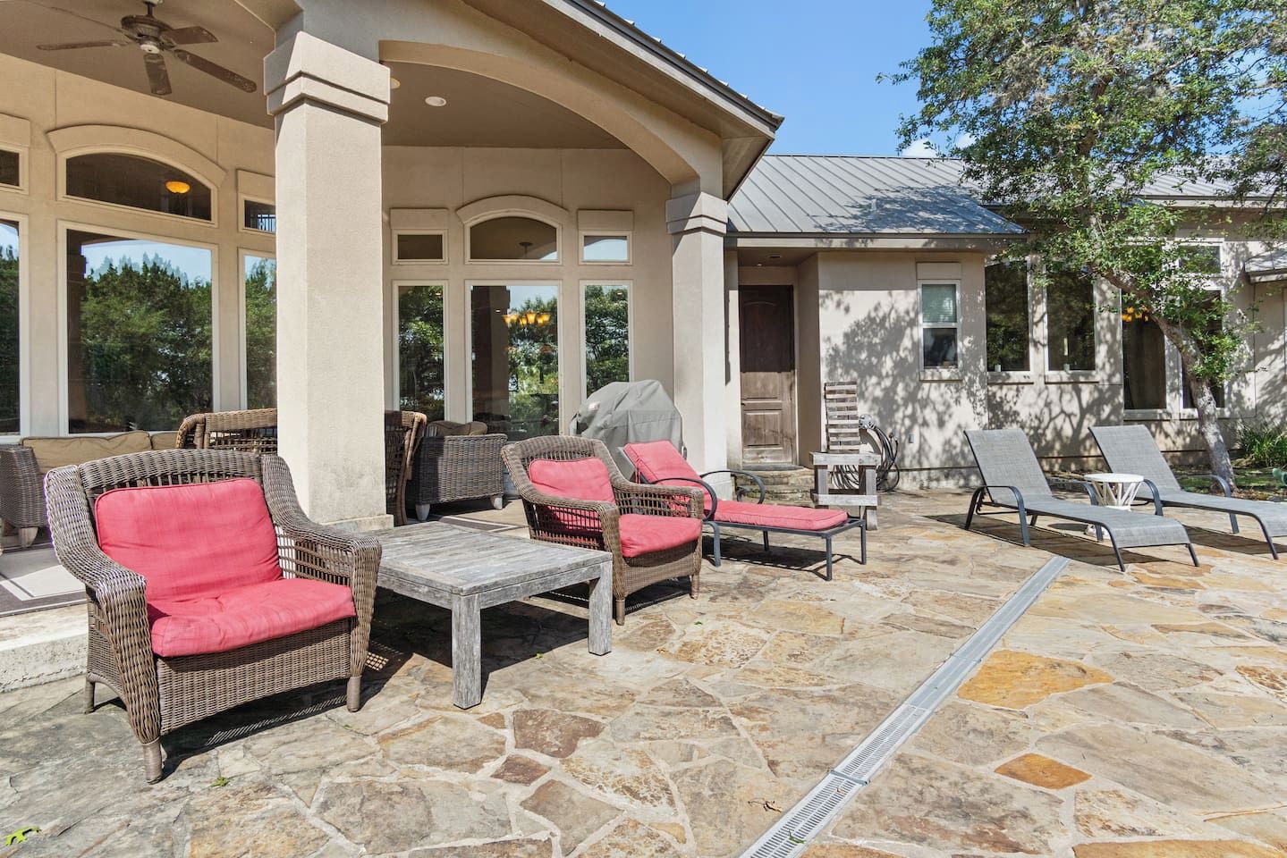 An outdoor patio with wicker furniture, a stone floor, and a covered area with columns.