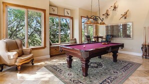 A pool room with a pool table, chairs, and a large window with a view of trees. - Rockin B Summit | Luxury Retreat with Pool & Creek (Pipe Creek)