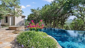 A swimming pool with a stone deck, surrounded by lush greenery and a mountain view. - Rockin' B Ranch Summit House (Pipe Creek)