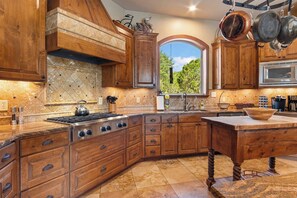 A kitchen with wooden cabinets, a stove, and a window with a view of greenery.