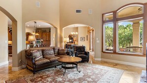 A spacious living room with a large sofa, a coffee table, and a view through a large window. - Rockin' B Ranch Summit House (Pipe Creek)