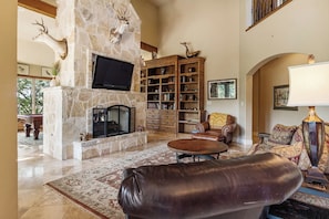 A spacious living room with a stone fireplace, leather furniture, and a bookshelf.