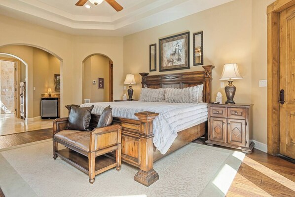 A bedroom with a large bed, a wooden nightstand, a chair, and a door.