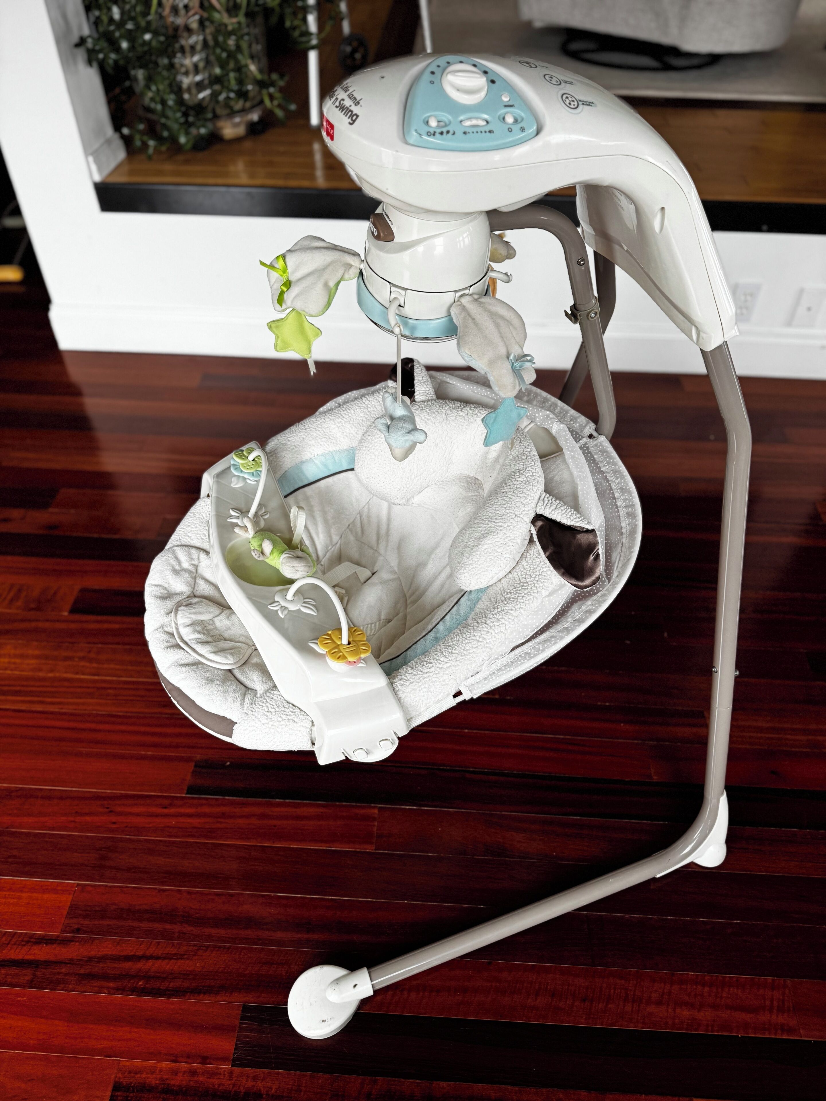 Un transat pour bébé, de couleur blanche et bleue, doté d’un plateau et d’un mobile suspendu.