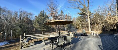 Eine Terrasse im Freien mit Tisch und Stühlen, umgeben von Bäumen und einem Holzzaun.