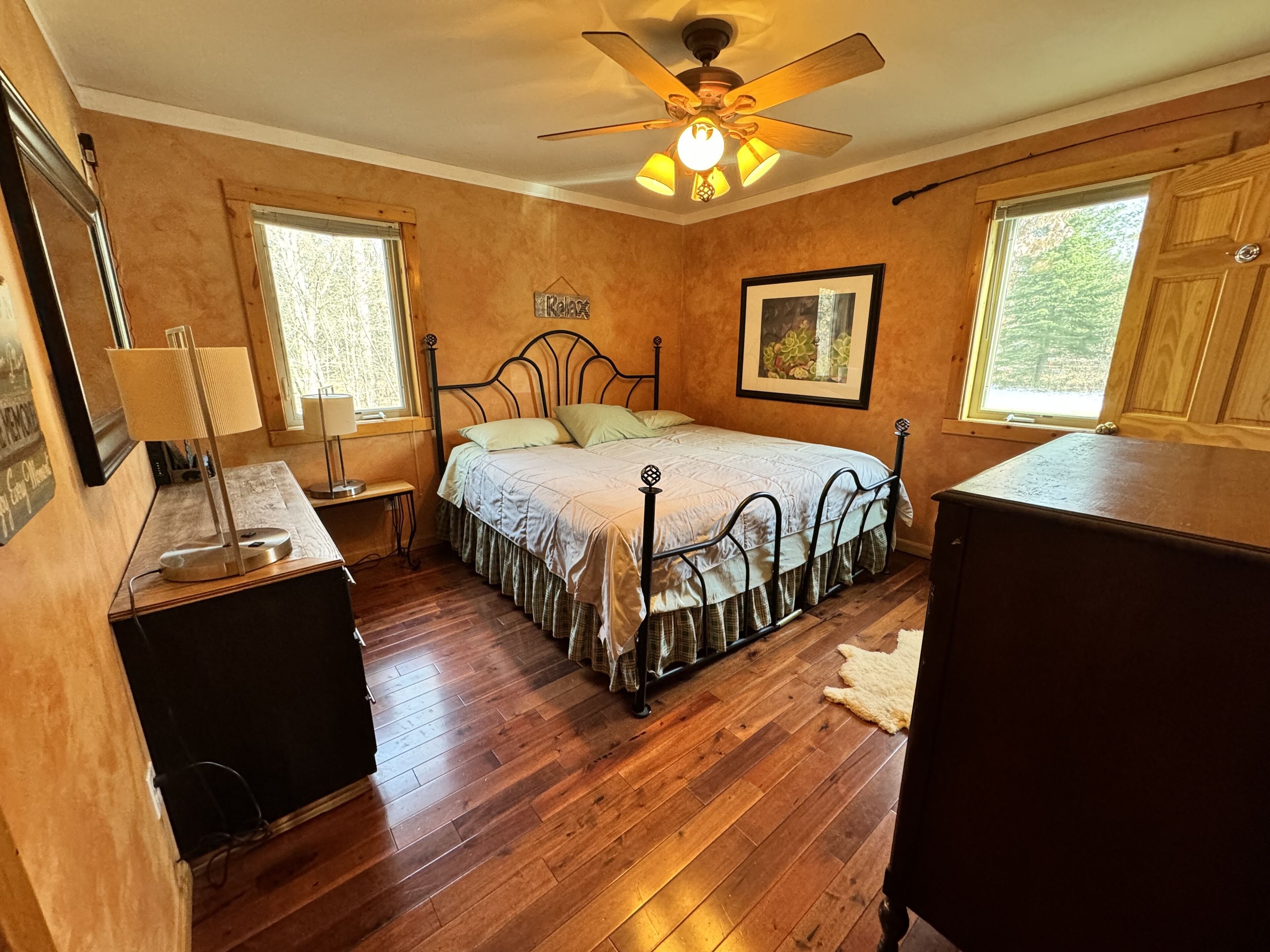 A bedroom with a bed, a ceiling fan, a desk, and a window.