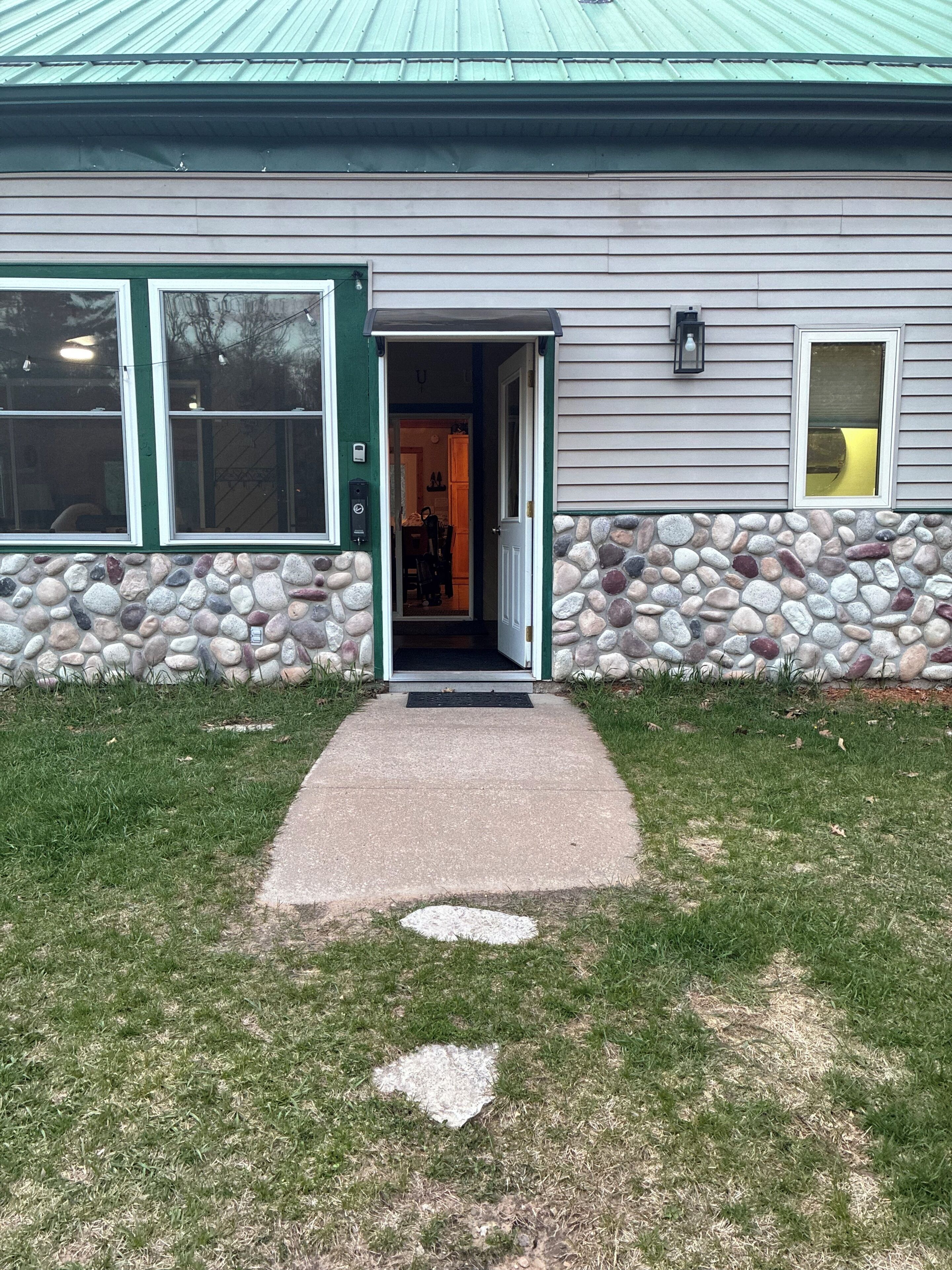 Un edificio con fachada de piedra, una puerta verde y un camino de concreto que lleva a la entrada.