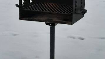 A black barbecue grill with a metal grate, standing on a metal pole in a snowy outdoor setting.