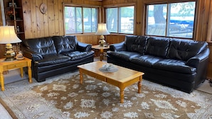 Ein gemütliches Wohnzimmer mit zwei schwarzen Ledersofas, einem Holztisch und einem gemusterten Teppich.