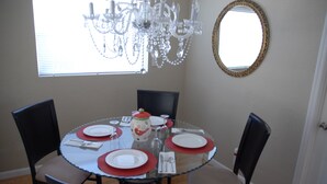 Un comedor con una mesa redonda preparada para cuatro personas, rodeada de sillas. Un candelabro cuelga del techo y hay un espejo en la pared.