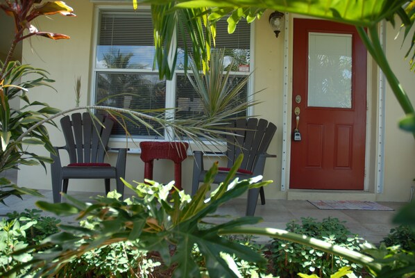 A front door with a red doorbell, a window with blinds, and two chairs with red cushions outside. - Home Away From Home/Pets Welcome (Wilton Manors)