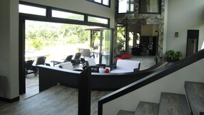 A spacious indoor area with a curved staircase, large windows offering views of greenery, and a seating area with sofas and chairs. - Beautiful Lake House outside of Medellin Colombia (55 Kilometers) (Amaga)
