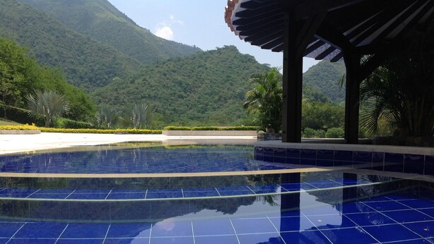 A swimming pool with blue tiles, surrounded by greenery and a mountain in the background. - Beautiful Lake House outside of Medellin Colombia (55 Kilometers) (Amaga)
