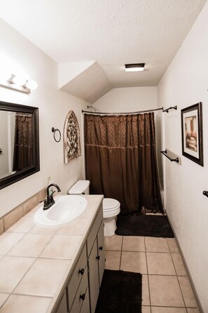 A compact bathroom with a sink, toilet, and shower curtain. - Casa Rio River House @ Casa Rio Rentals- River Front, Pet Friendly in Concan (Concan)