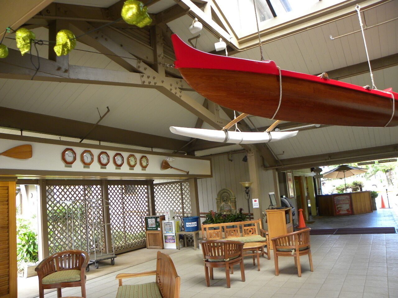 A covered outdoor seating area with wooden furniture, a red boat hanging from the ceiling, and a donation box.