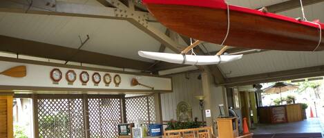 A covered outdoor seating area with wooden furniture, a red boat hanging from the ceiling, and a donation box.