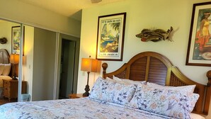 A bedroom with a floral bedspread, a wooden headboard, a ceiling fan, and a poster on the wall. - PERFECT KAUAI Condo!! Steps from Beach/2bd2bth Washer/Dryer AC -Free Parking (Kapaa)