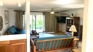 A living room with a wooden sofa, a television, and a ceiling fan. - PERFECT KAUAI Condo!! Steps from Beach/2bd2bth Washer/Dryer AC -Free Parking (Kapaa)
