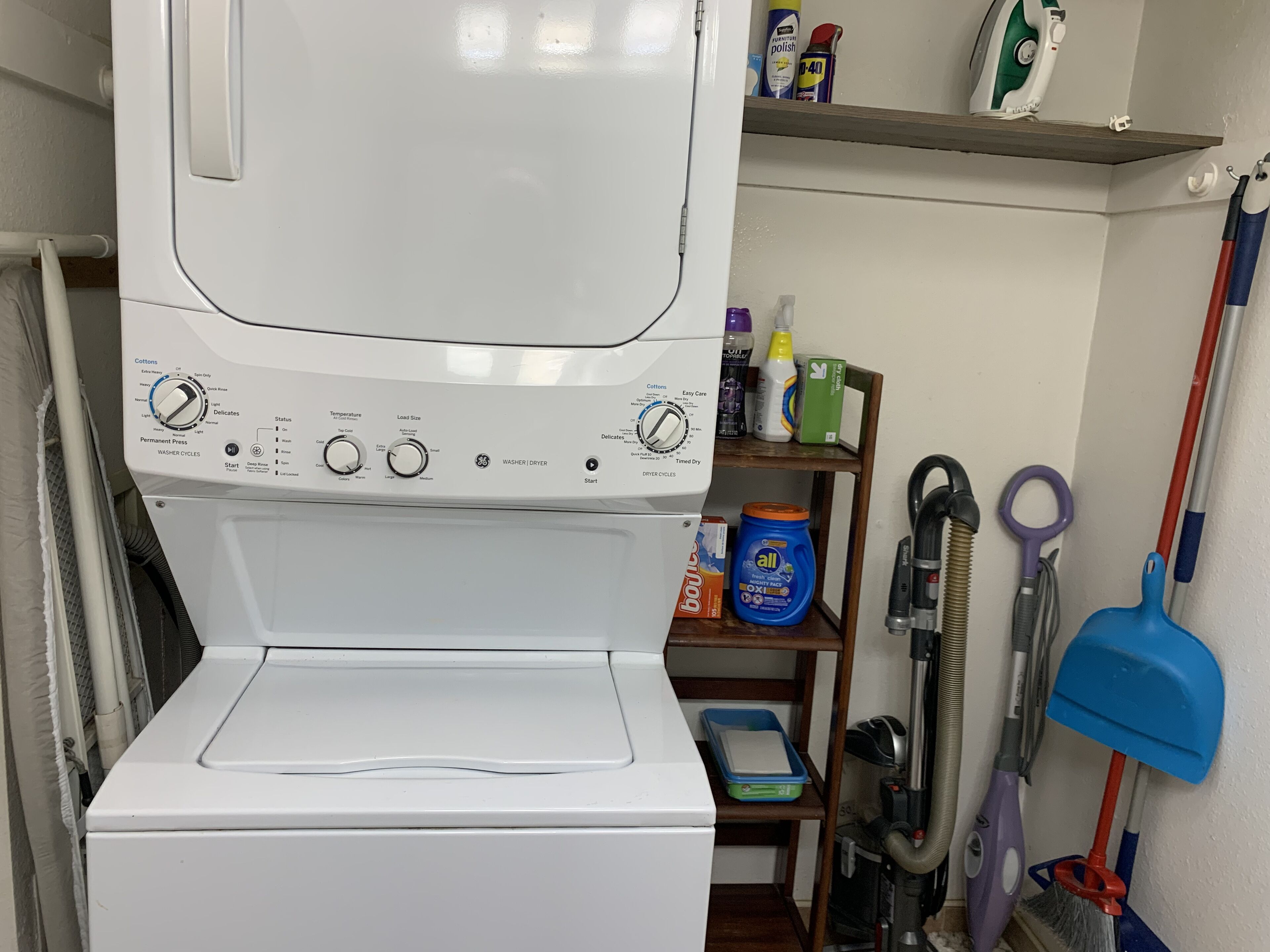 Eine Waschmaschine mit Frontlader, ein Reinigungsmittelregal und ein Staubsauger.