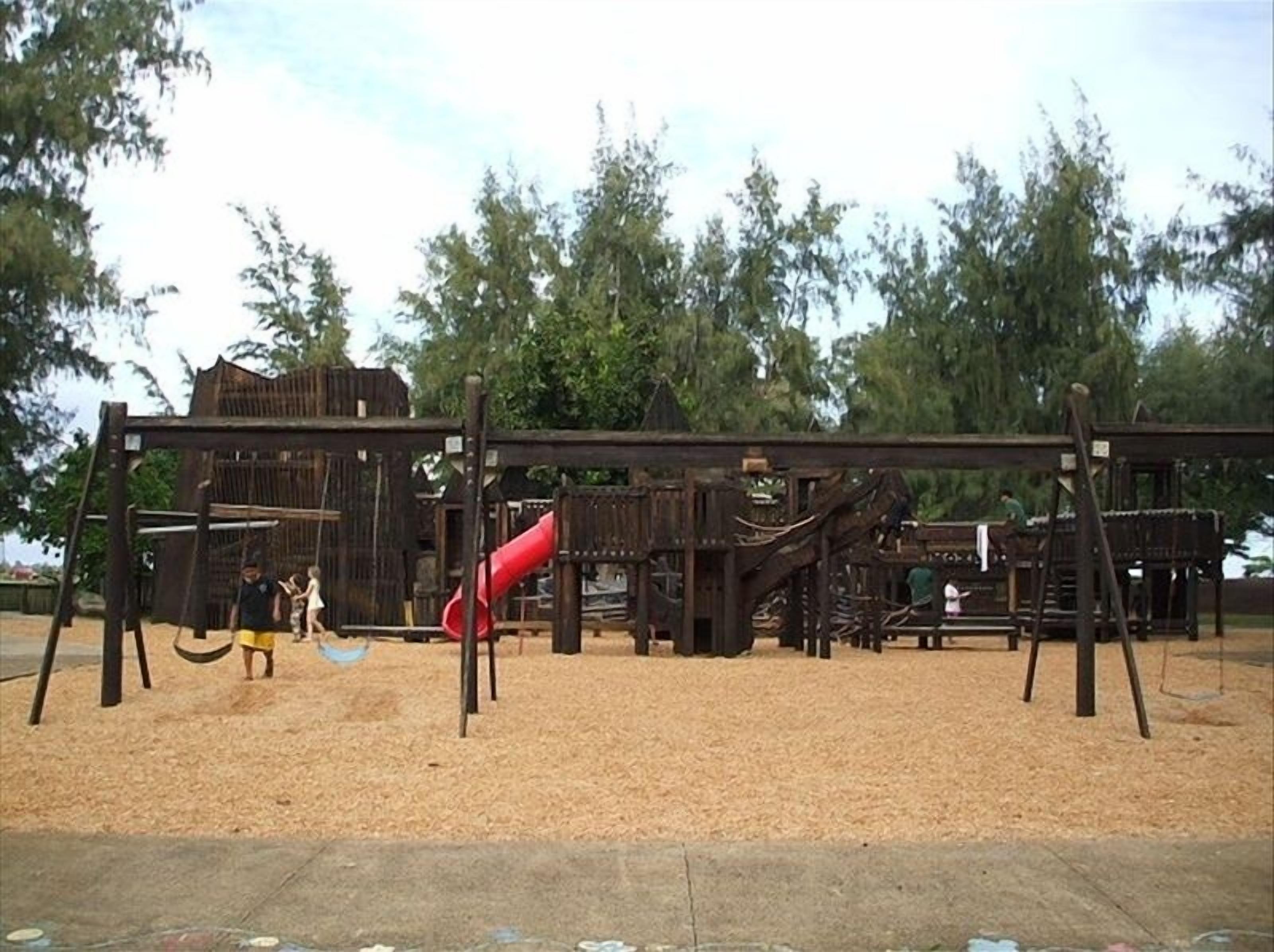 Ein Spielplatz mit Holzkonstruktionen und einer roten Rutsche.