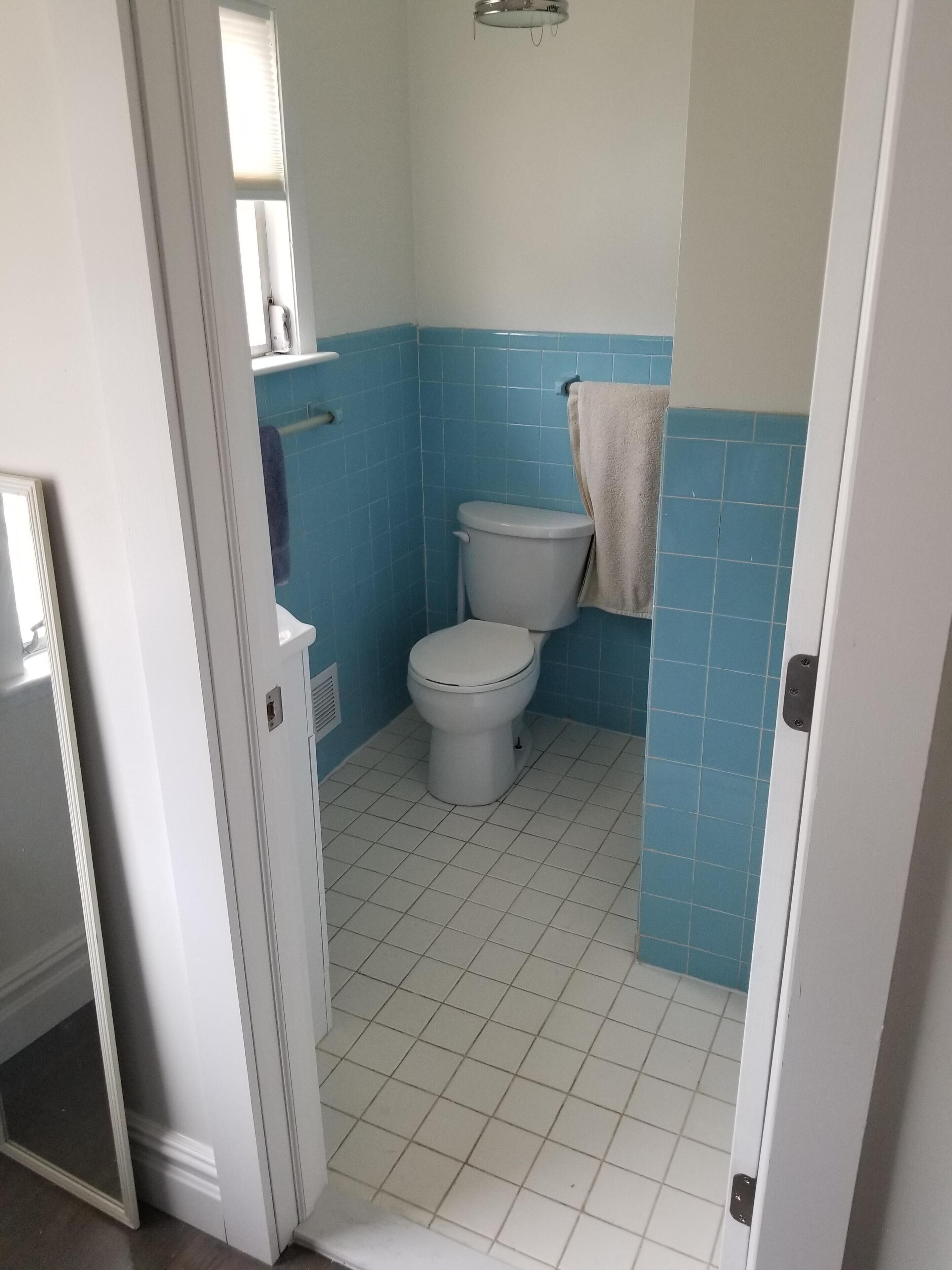 A bathroom with a toilet, a towel hanging on the wall, and a window with blinds.