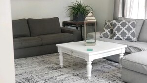 Ett vardagsrum med ett vitt soffbord, en grå soffa och en mönstrad prydnadskudde.