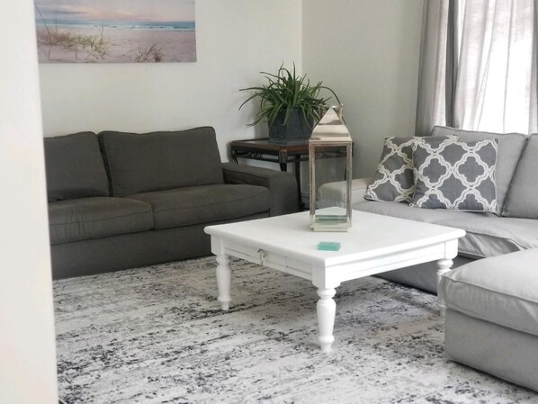A living room with a white coffee table, grey sofa, and a patterned throw pillow. - 4 min walk to famous Seaside Heights boardwalk.Quiet family neighborhood . (Seaside Heights)