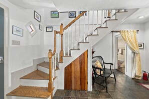 A staircase with wooden steps and white railings, a black chair with a giraffe-patterned cushion, and a fire extinguisher on the floor.
