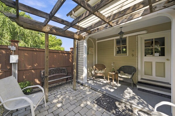 A covered patio with a wooden pergola, outdoor seating, and a door leading to a house.