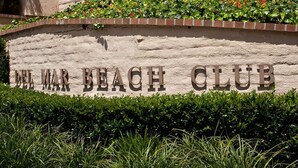 Une enseigne pour le Del Mar Beach Club, avec une bordure en briques et une haie devant.