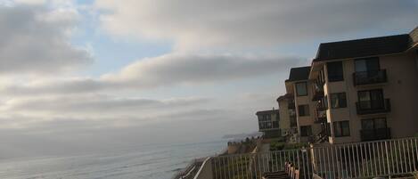 A coastal balcony with wooden benches and a railing overlooking the sea.