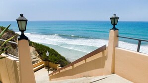 Un escalier qui descend vers la côte et mène à une plage offrant une vue sur l’océan, agrémenté de lampadaires et d’une rambarde.