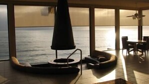 Un salon moderne doté d’une grande fenêtre donnant sur la mer, d’une table ronde et d’un ventilateur de plafond.