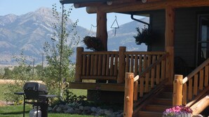A wooden cabin with a porch, a grill, and a mountain backdrop.