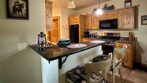 A kitchen with wooden cabinets, a black refrigerator, a microwave, a stove, and a hanging light fixture.