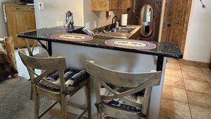 A kitchen with a central island, two bar stools, wooden cabinets, a mirror, and a television.