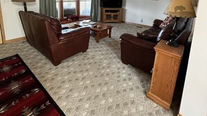 A living room with a brown leather sofa, a wooden coffee table, a television on a stand, a patterned rug, and a window with curtains. - EMIGRANT LODGE - 4 bedroom home with central airconditioning (Emigrant)