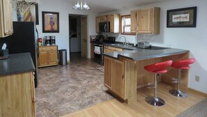 A kitchen with wooden cabinets, a stainless steel sink, a microwave, and a toaster. There is a bar area with red stools. - EMIGRANT LODGE - 4 bedroom home with central airconditioning (Emigrant)