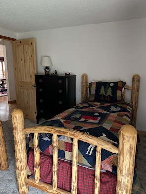 A bedroom with a wooden bed frame, a quilted bedspread, a wooden dresser, and a nightstand with a lamp.