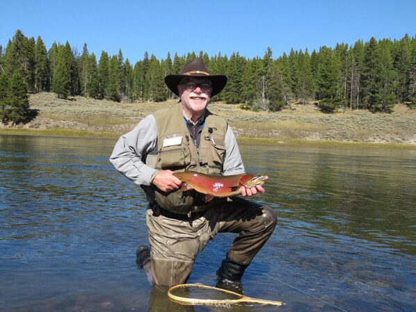 A person holding a fish in a river surrounded by trees.