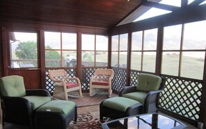 A covered porch with wicker furniture, a glass table, and a view of a grassy area.