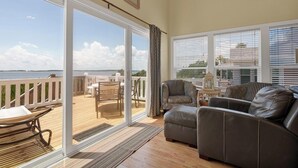 A spacious living area with a large sliding glass door leading to a deck overlooking a body of water. There is a leather sofa and a small table with a lamp. - RARE 6 bedroom, 4 bath OCEANFRONT home, wonderful views & breathtaking sunsets! (Edisto Beach)