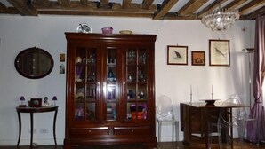 Een kamer met zichtbare houten balken, een houten kast met glazen deuren, een ronde spiegel en een kroonluchter.