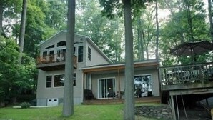 A two-story house with a balcony, a covered deck, and a stone wall in the foreground.