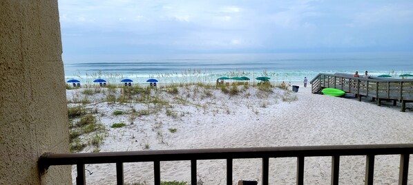 A beach view from a balcony with a wooden deck, beach umbrellas, and a sandy shoreline.