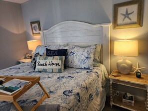 Cozy bedroom with a white headboard and floral-patterned bedspread, featuring two pillows and a nightstand with a lamp and decorative starfish.