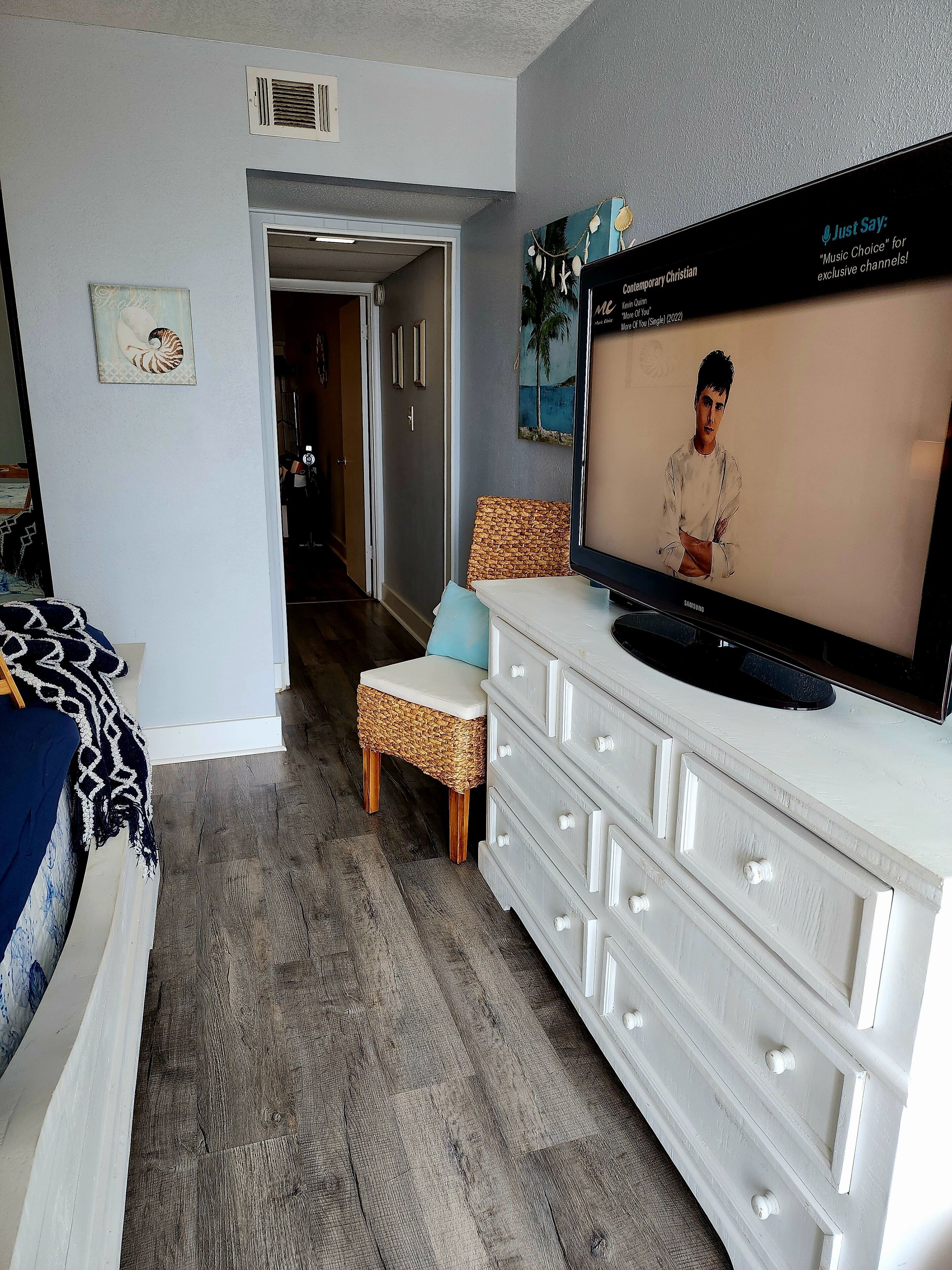 Una sala de estar moderna con una televisión, una silla de mimbre, un aparador blanco y un pasillo que conduce a otra habitación.