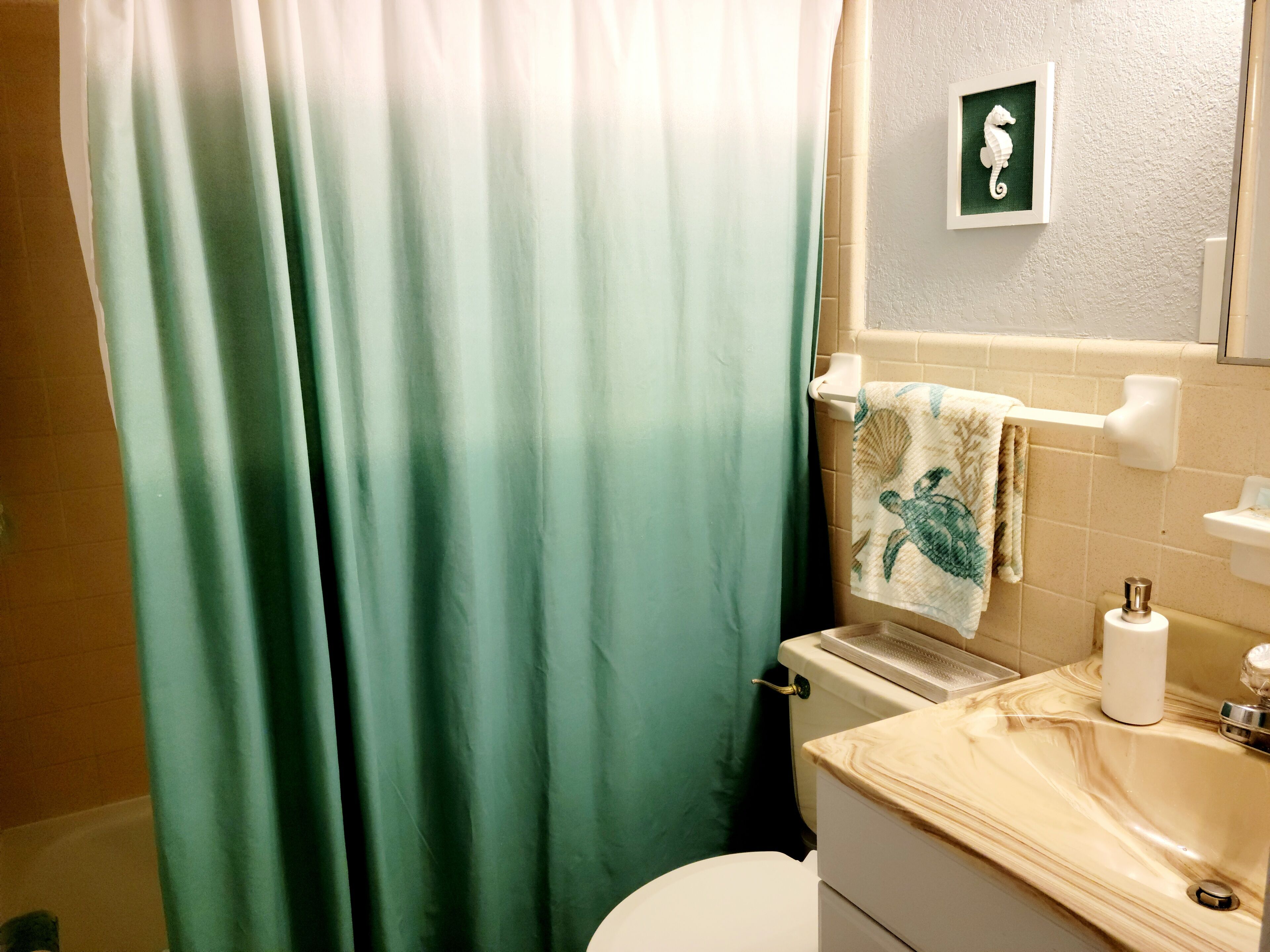 Een badkamer met een groen douchegordijn, een toilet, een wastafel met een marmeren blad en een handdoekrek met een handdoek.