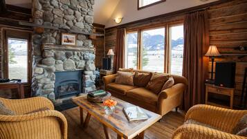 A cozy living room with a stone fireplace, wooden furniture, and a view of mountains.