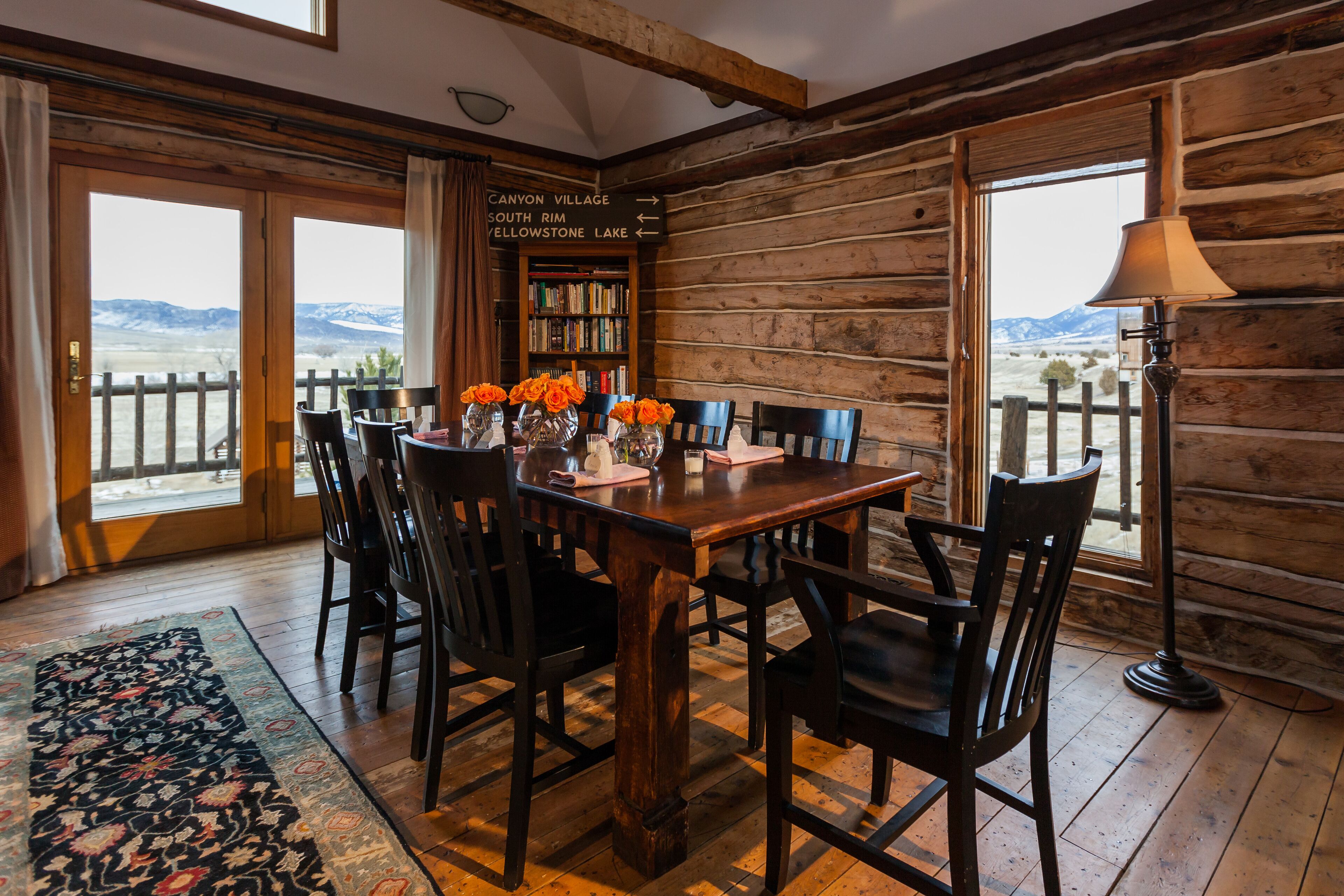 A wooden interior with a dining table, chairs, and a view of the mountains through large windows.